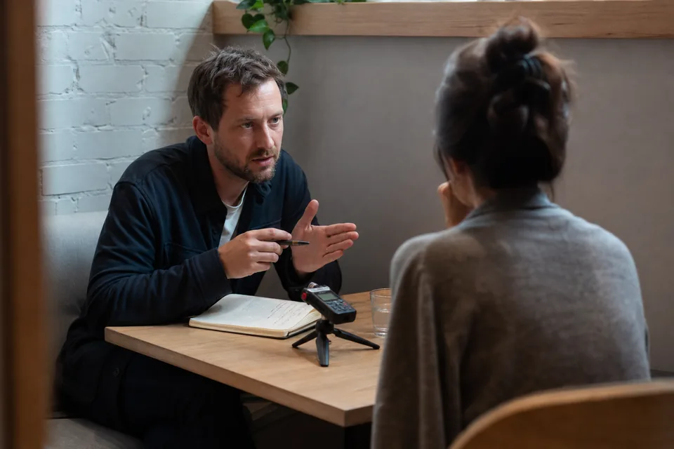 Founder talking with a customer across a small table with a phone recording the conversation