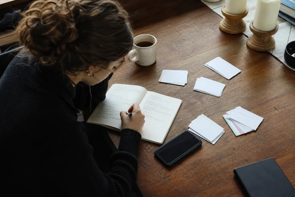 Hand writing a list of survey questions in a notebook next to grouped index cards