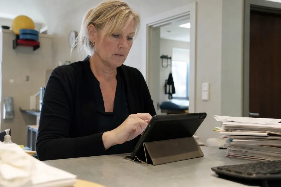Clinic manager preparing a tablet questionnaire at the front desk next to old paper forms