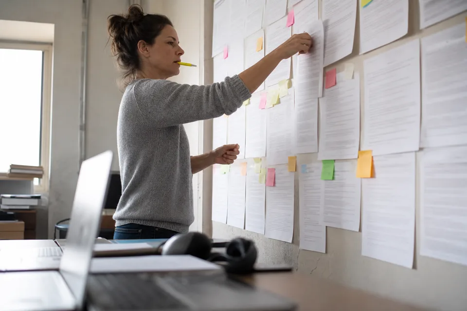 Researcher grouping printed answer transcripts into themes on a wall of sticky notes