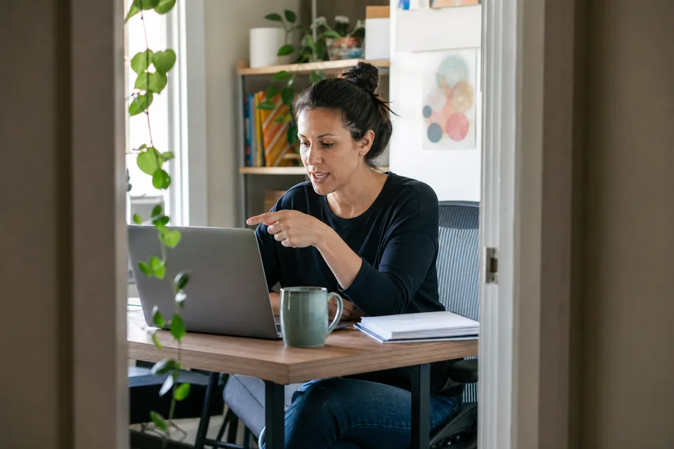 Product user recording video feedback with her laptop webcam in a home office corner